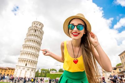 Young female traveler smiling in front of the famous leaning tower in Pisa old town in Italy